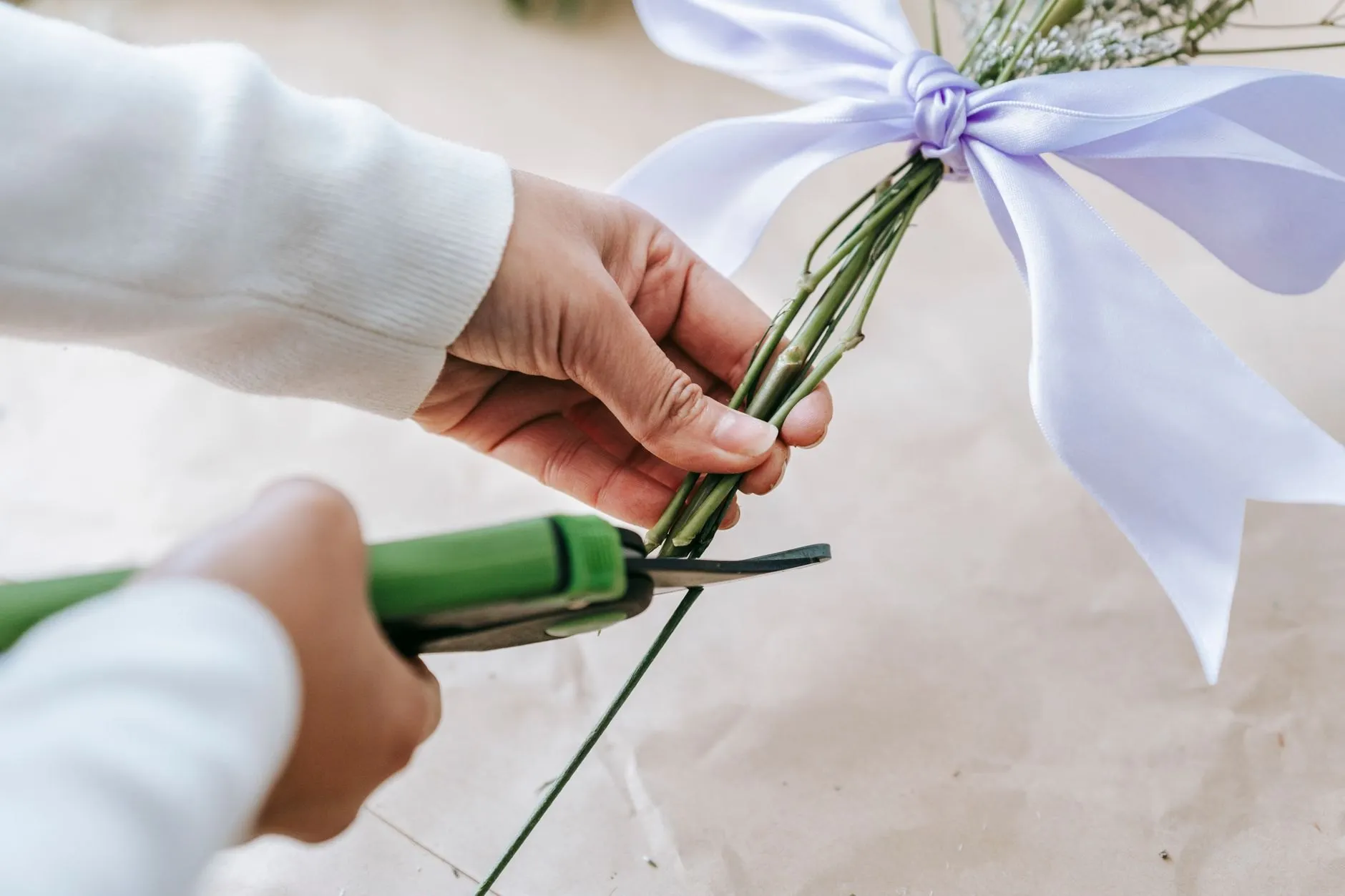 Pruning shears cutting green stems at an angle on a kraft-paper bench