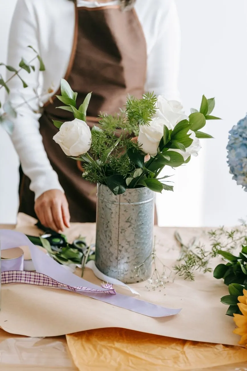 White roses and greenery arranged in a zinc vase on the bench