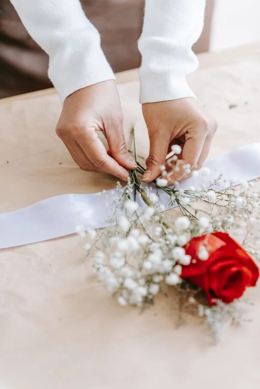 Hands tying a satin ribbon around a posy on kraft paper
