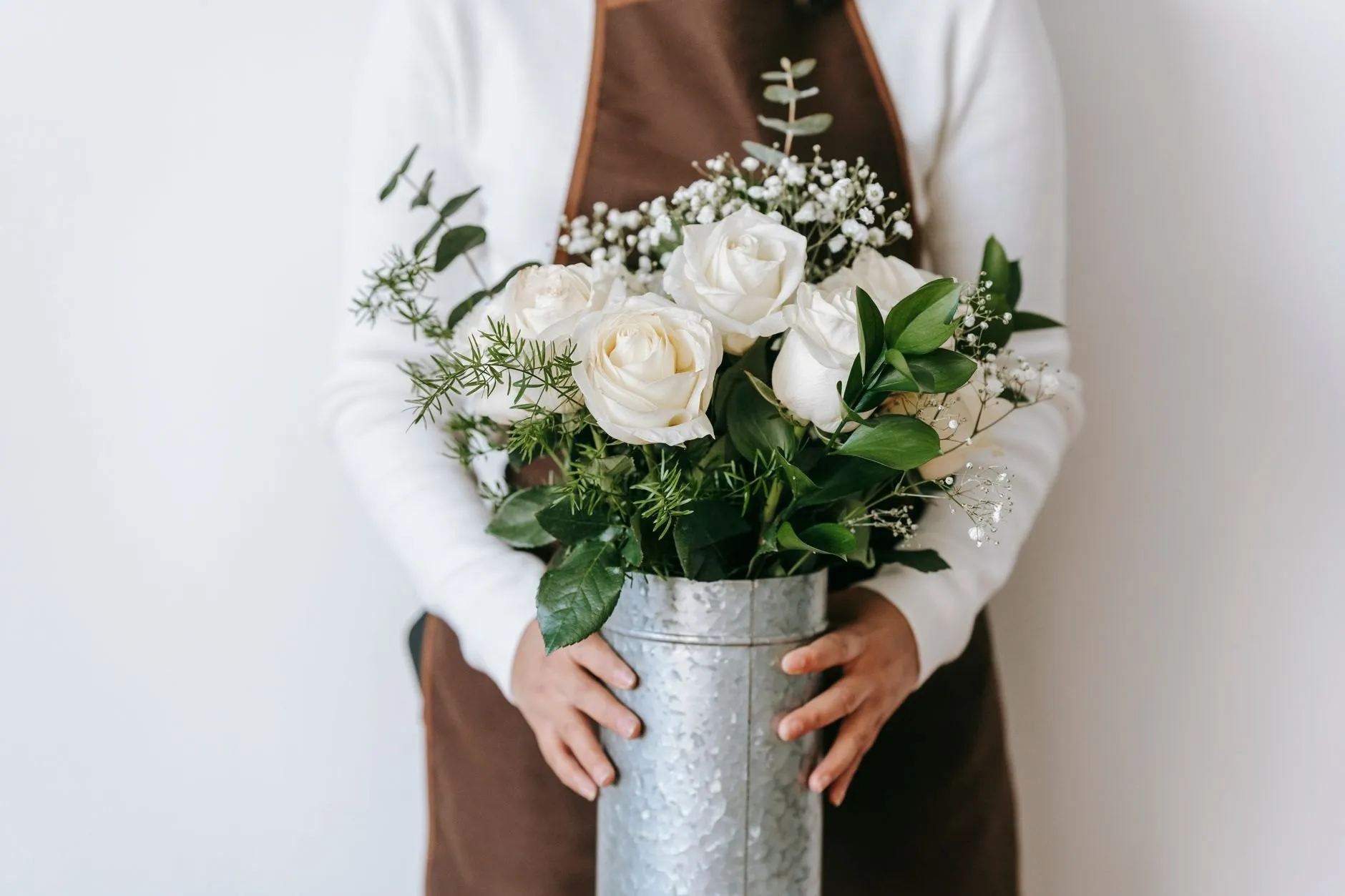 White roses and greenery arranged in a zinc vase held in both hands